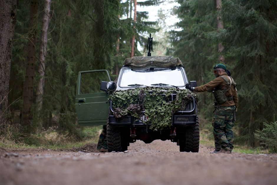 Soldier in camouflage operates an armored vehicle in a dense forest, showcasing military readiness.