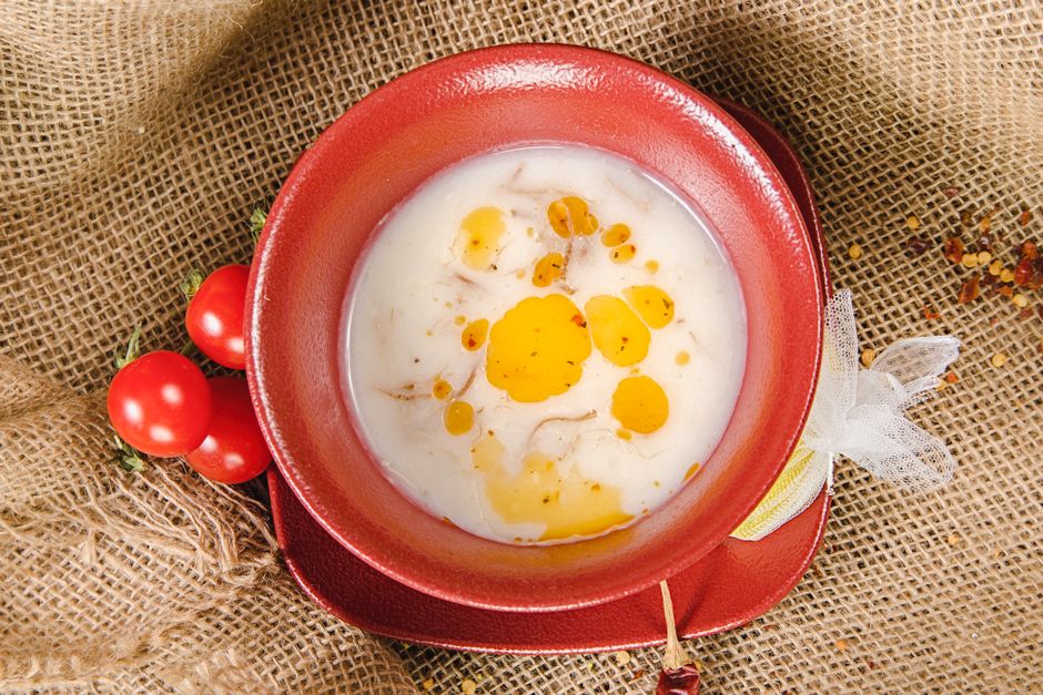 Top view of creamy red lentil soup with tomatoes and olive oil in a red ceramic bowl on a burlap background.