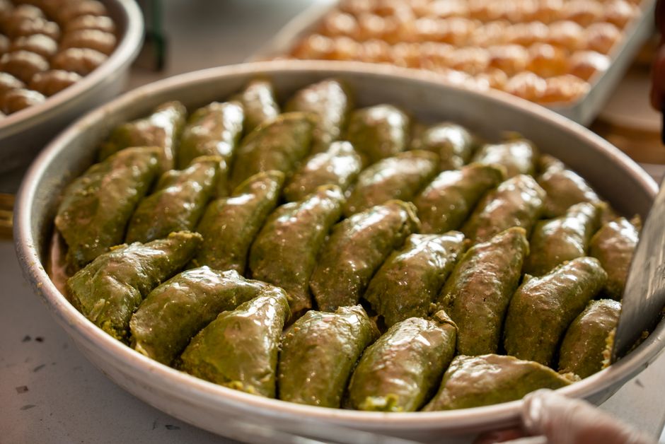 Close-up of freshly prepared pistachio baklava in a large silver tray under soft lighting.