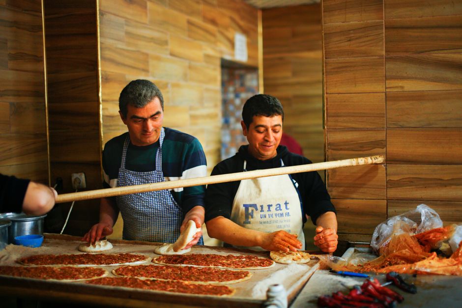 Two cooks preparing traditional Turkish lahmacun in a kitchen, showcasing craftsmanship.